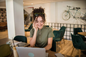 A young woman is working on a laptop while sitting in a cafe and drinking a frappe coffee that is on the table - RQTech AI-powered customer engagement solutions