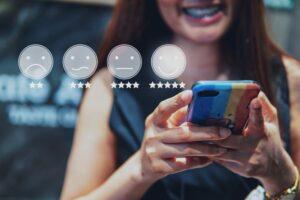 Picture1 - RQTech Close-up of hands holding a smartphone with a translucent rating row: four circular emoticons from sad to happy and a row of stars beneath each.